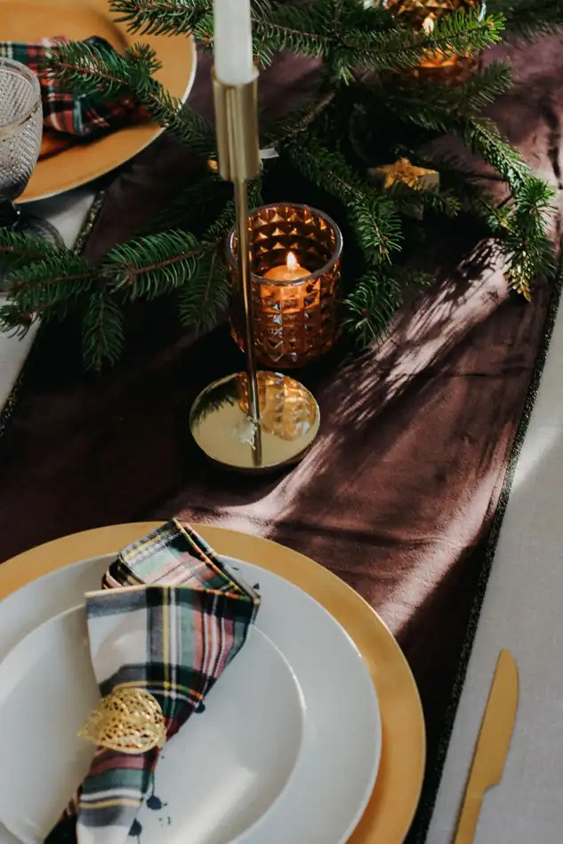 A candlelit Christmas table with evergreen branches and carefully set places